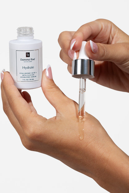 Hand holding a dropper with skincare serum next to a bottle labeled 'Hydrate'. Hyaluronic and Beta Glucan Hydrating serum for Dry Skin